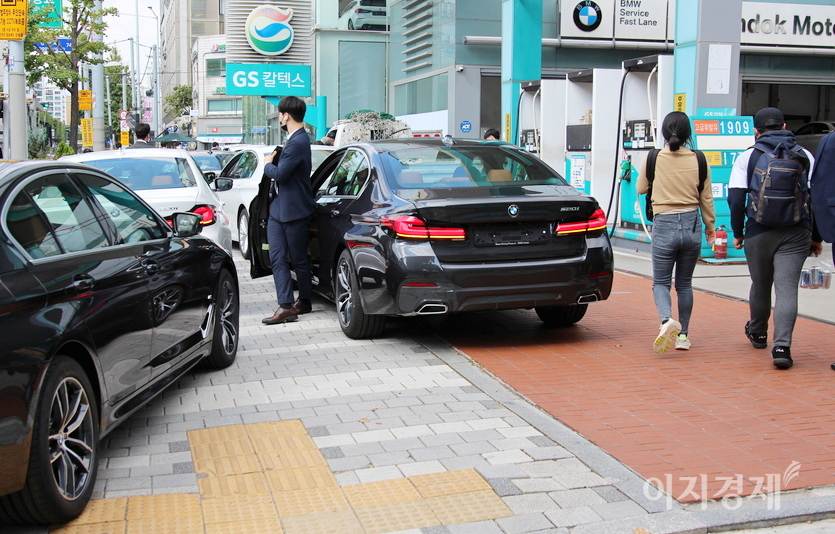 BMW그룹코리아(대표이사 한상윤)의 공식딜러 한독모터스(대표 박신광)가 운영하는 서울 방배전시장에 고객이 구입한 차량이 들어오고 있다. 번호판이 없는 BMW 차량이 인도를 점렴해 행인들은 차를 피해 주유소 땅으로 걸어가고 있다. 사진=정수남 기자